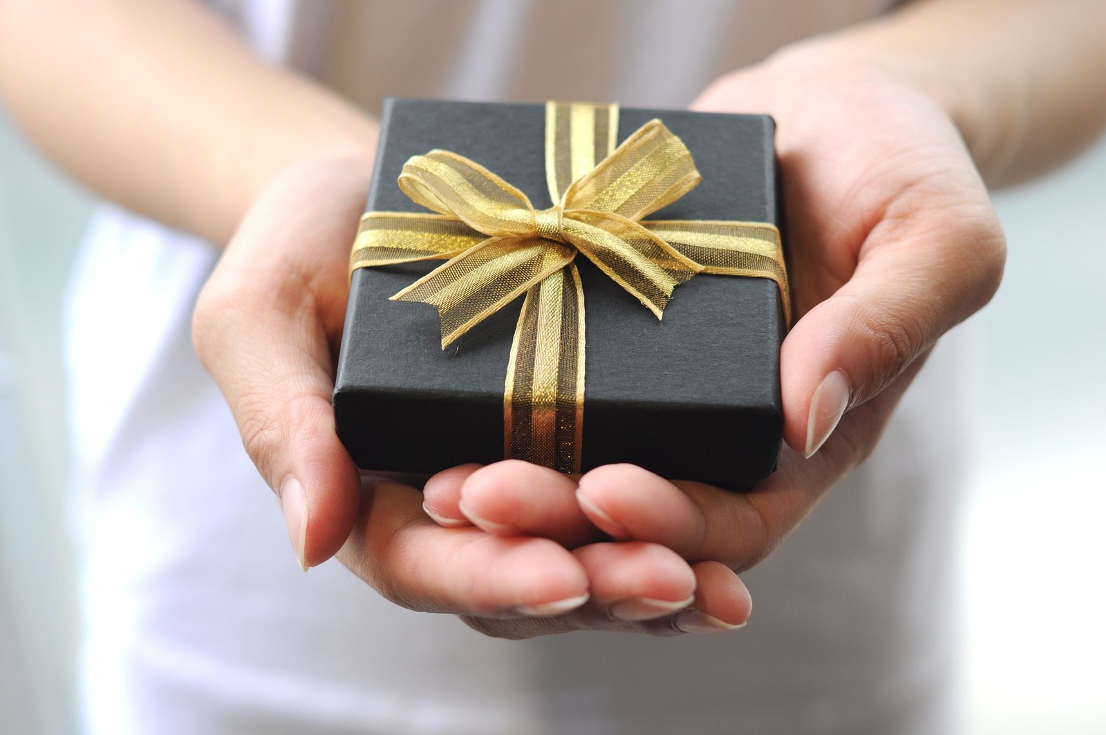 Un cadeau emballé d’un ruban doré est tenu entre deux mains.
