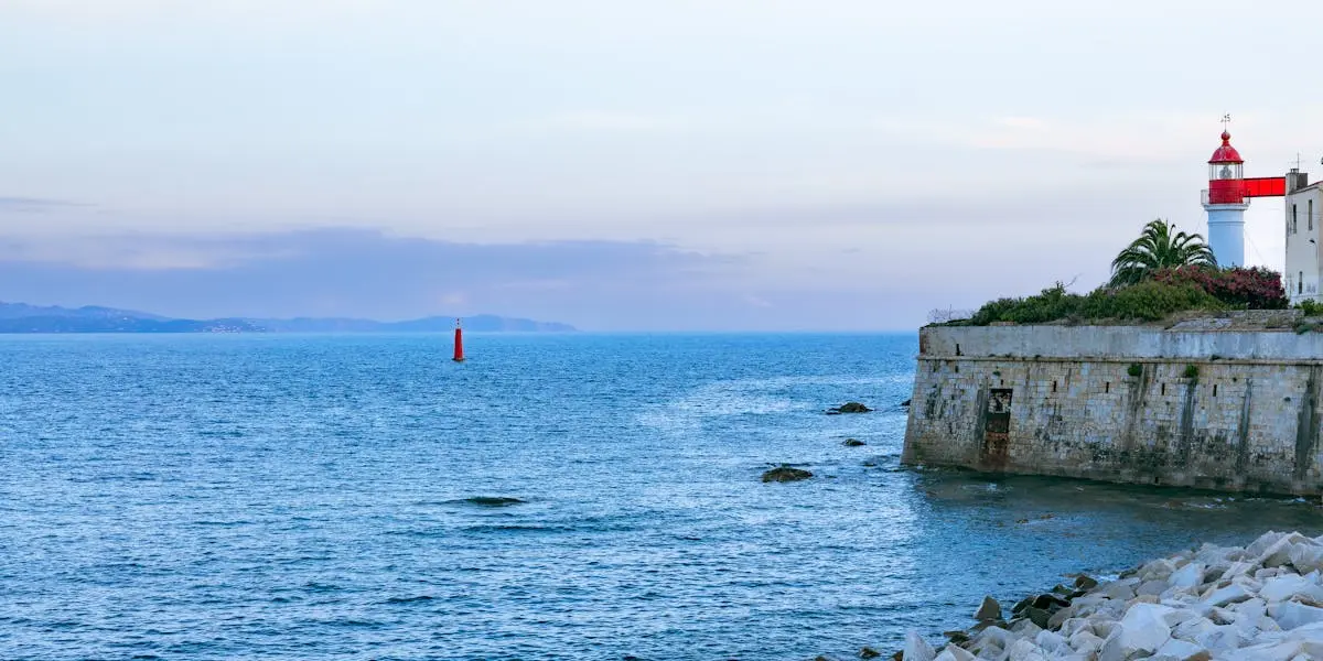 A scenic view of a lighthouse by the ocean in Ajaccio, Corsica during a serene sunset.