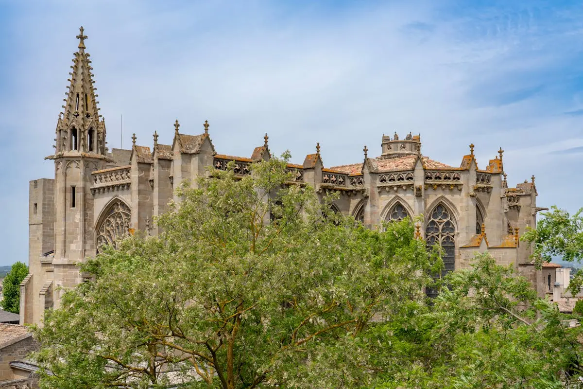 Stunning Gothic cathedral surrounded by lush trees under a bright blue sky, showcasing architectural splendor.