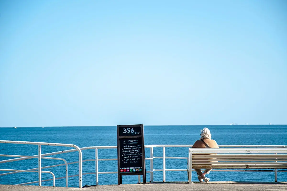 Elderly woman enjoying a sunny day on a bench by the sea in La Baule, France.