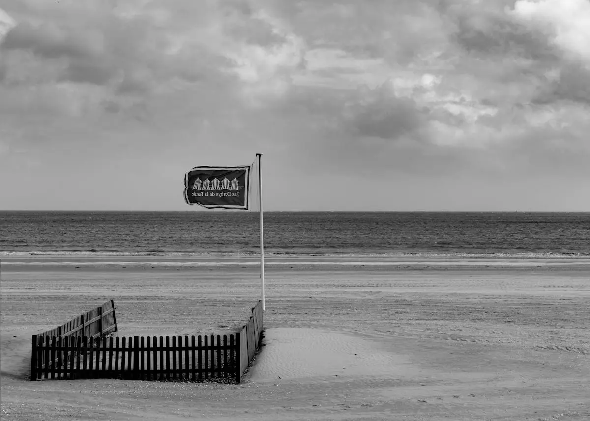 A serene black-and-white view of La Baule beach with a flag and fence, capturing tranquility.