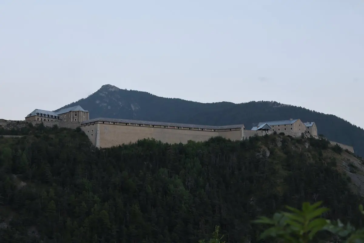 A historic fort perched on a hill in Briançon, France, surrounded by lush greenery.