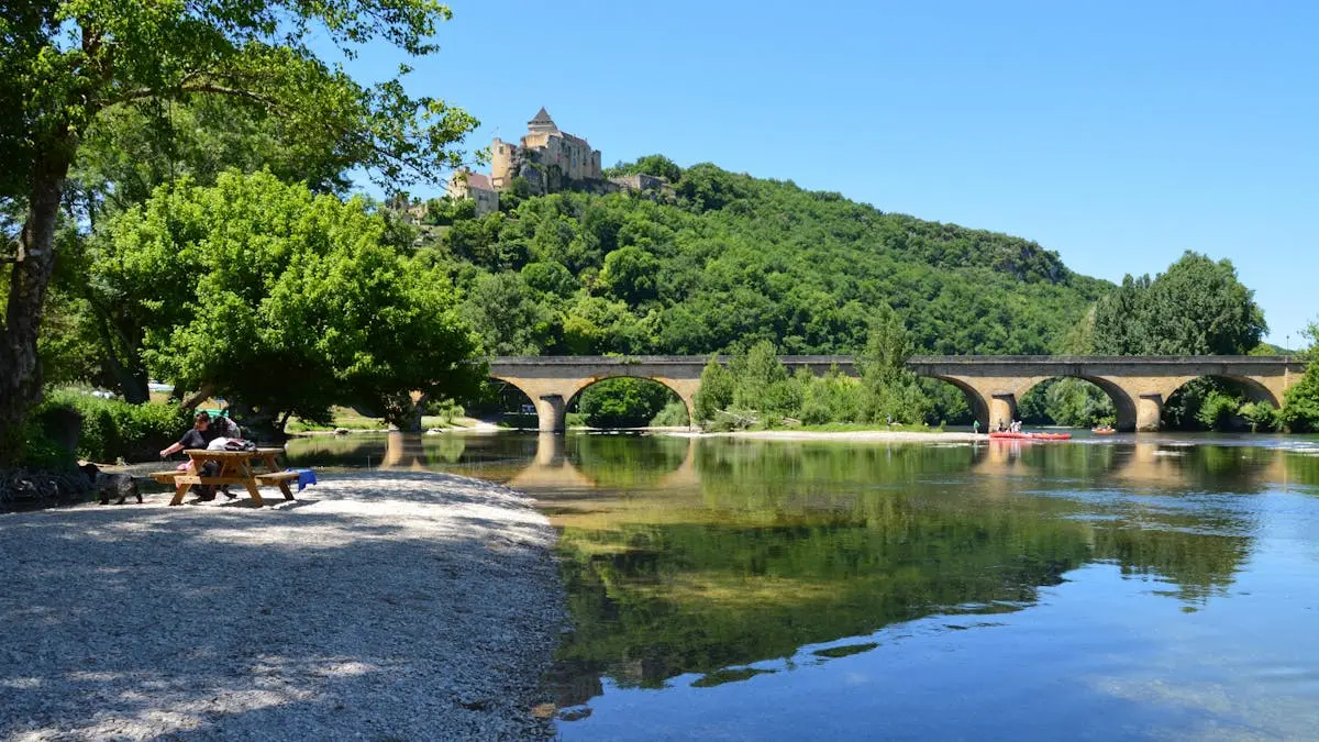 Picturesque view of Château de Castelnaud, bridge, and serene river in summer