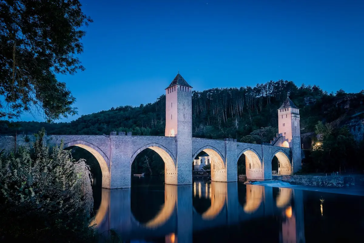 Stunning night view of the illuminated Pont Valentré reflecting in the Lot River, Cahors, France.