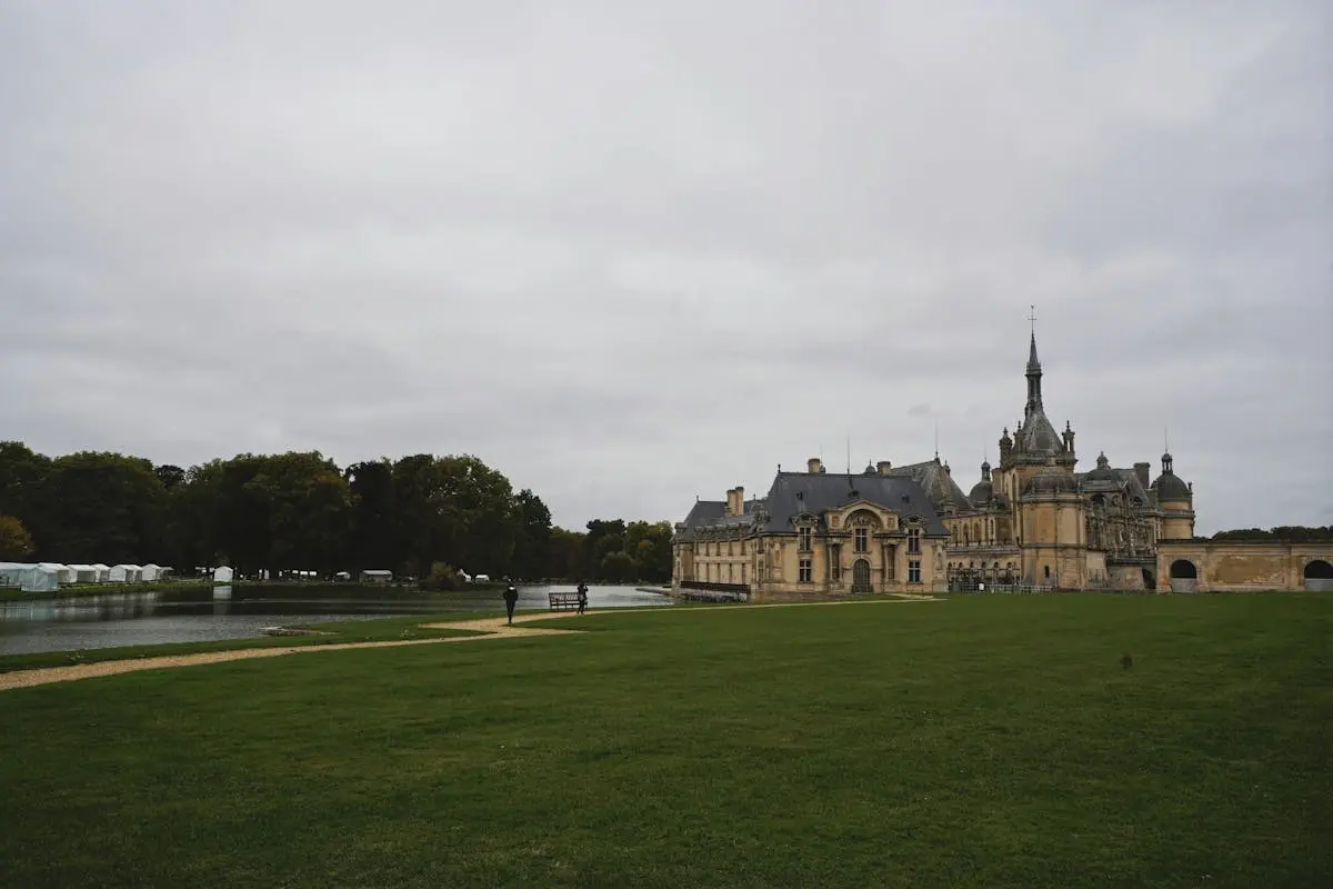 Château de Chantilly surrounded by lush greenery and overcast skies, showcasing classic French architecture.