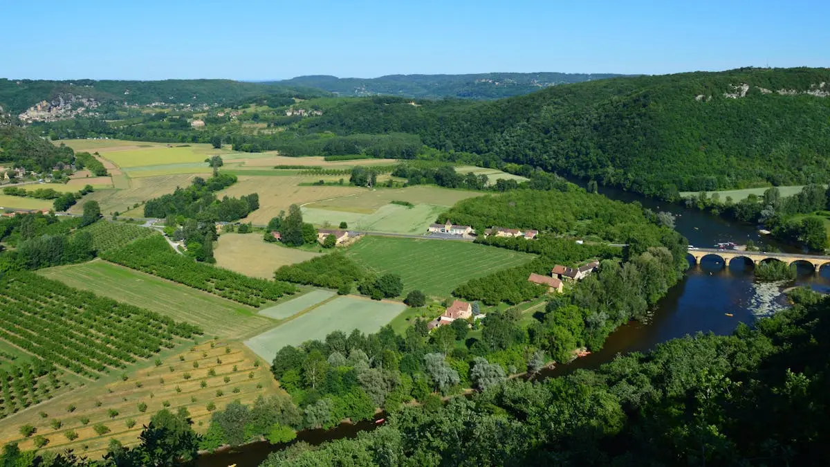 Aerial view of lush green fields, river, and a historical stone bridge in a rural setting.