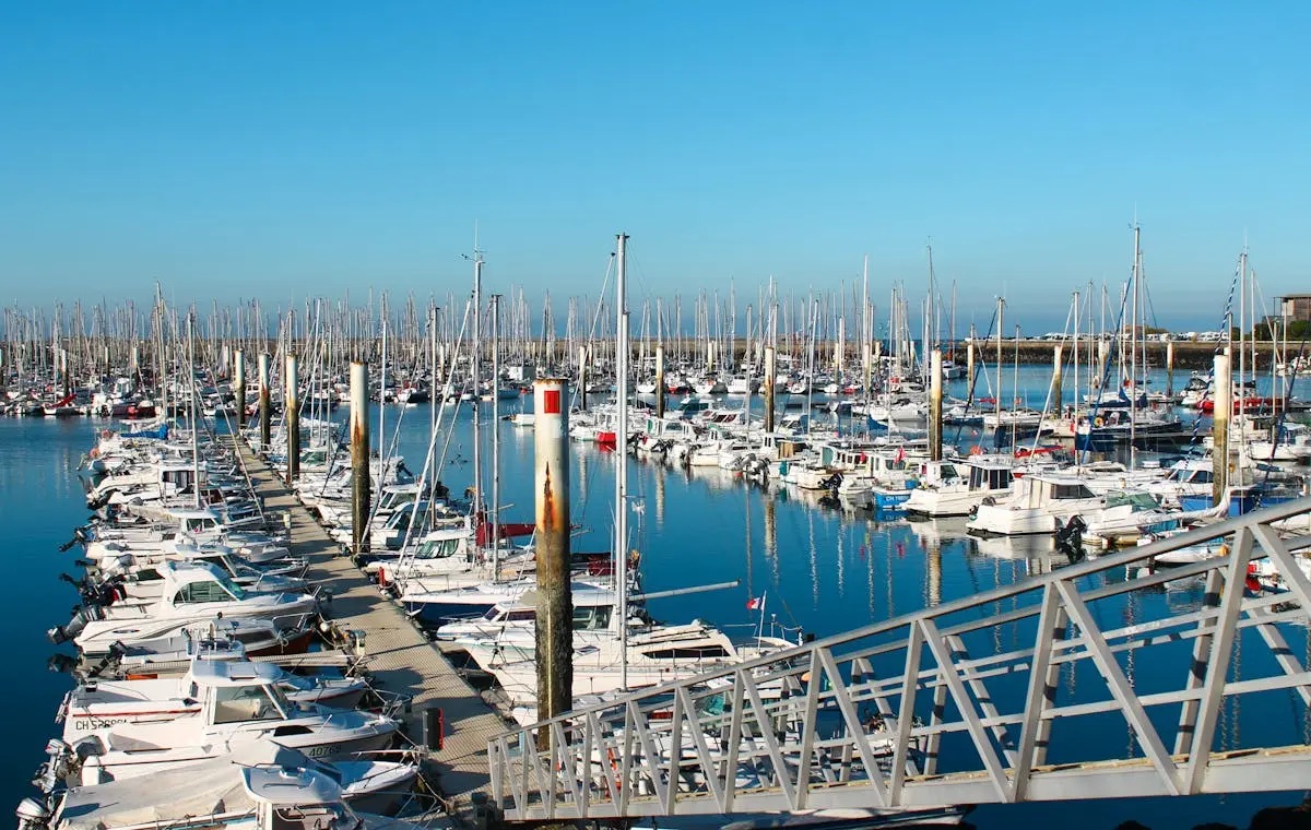 A bustling marina with numerous sailboats in Cherbourg, reflecting in calm waters under a clear blue sky.