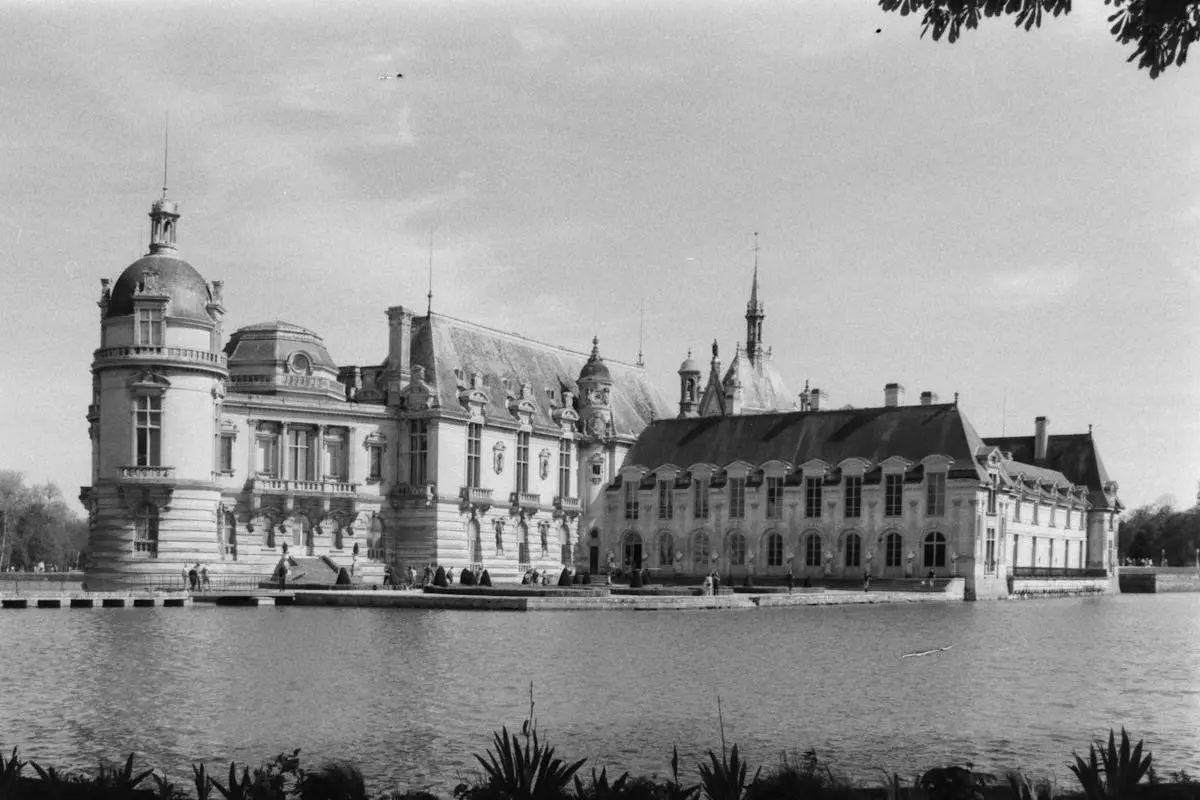 Black and white photo of the Château de Chantilly, France, reflected in a pond.