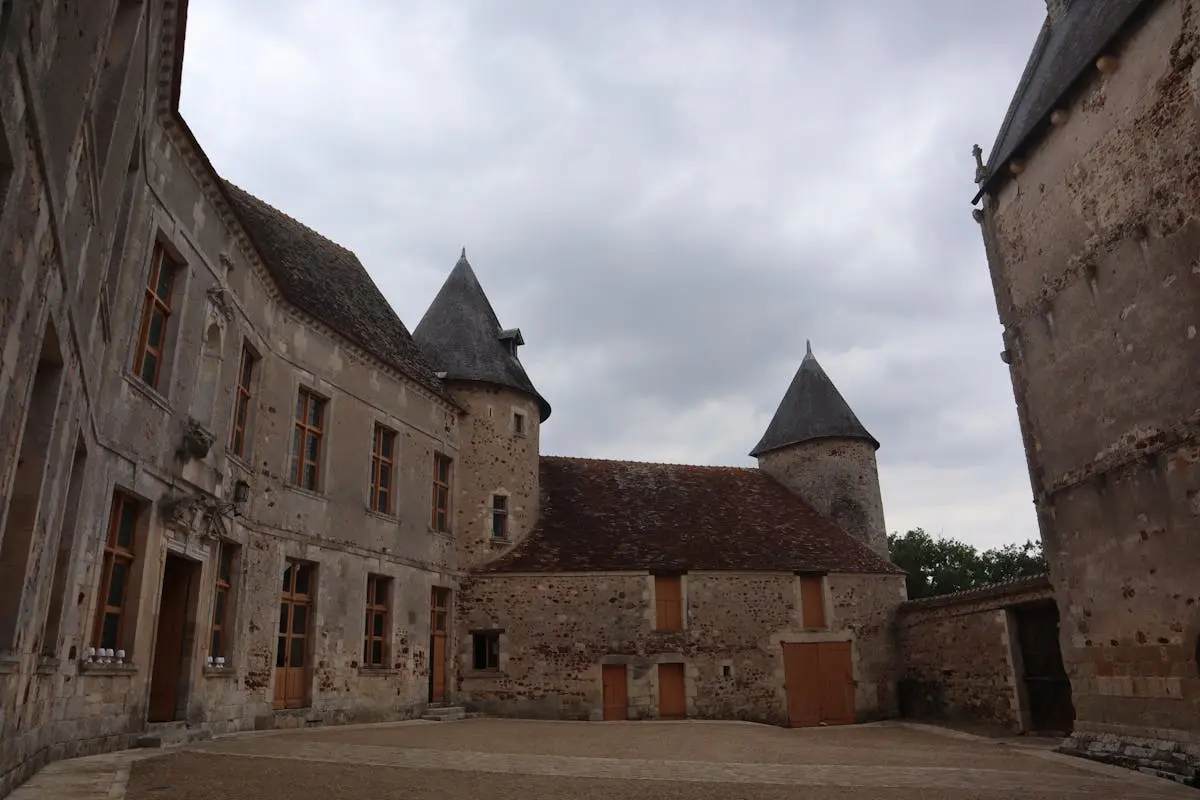 A historic castle courtyard in Rosnay, France, showcasing medieval stone architecture under a cloudy sky.