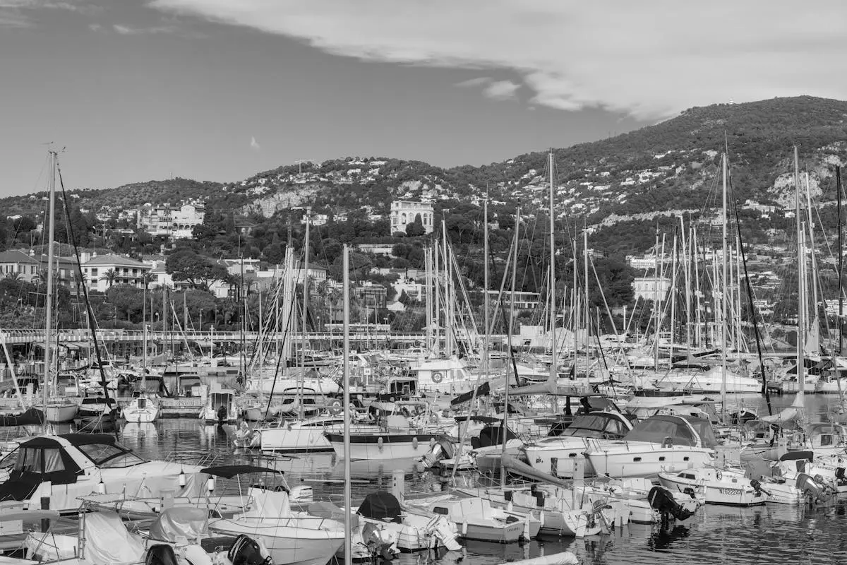 Black and white image of a marina filled with boats against a hillside backdrop in Beaulieu-sur-Mer, France.