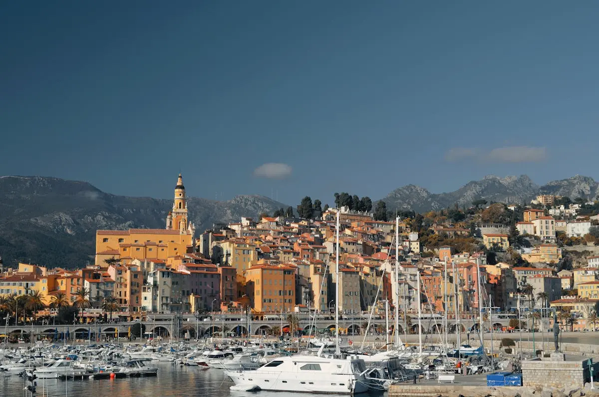 Explore the picturesque harbor of Menton, France with colorful buildings and boats under a clear blue sky.