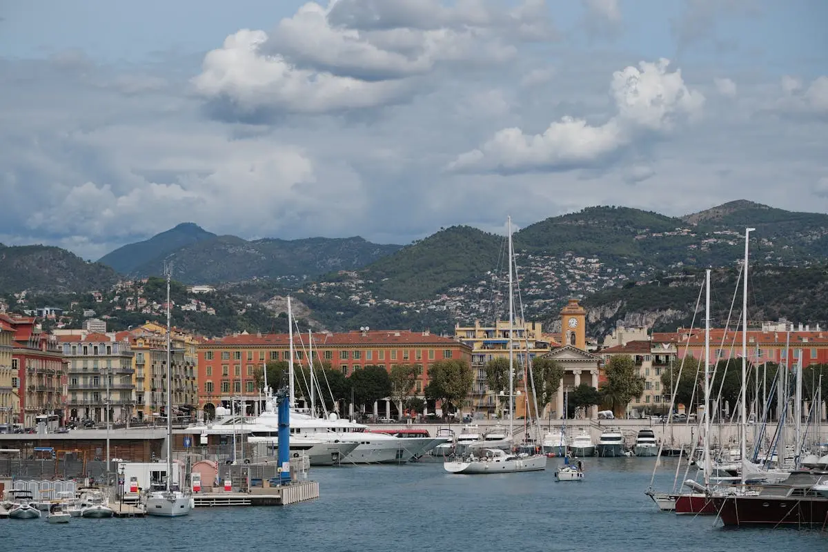 Scenic view of Port Lympia in Nice, France, featuring yachts, mountains, and classic architecture.