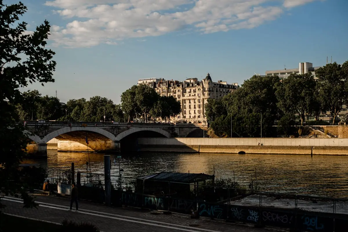 A scenic view of a Parisian bridge and riverbank under warm evening light.