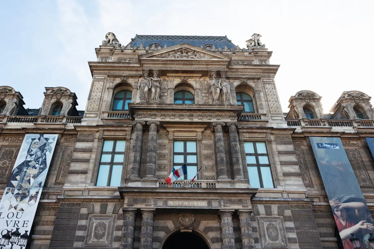 Architectural detail of the Louvre Museum showcasing French flags in Paris, France.