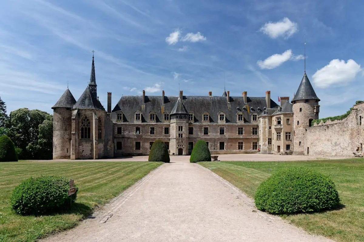 Historic Château de Lapalisse with gothic architecture set in a lush landscape under a bright sky.