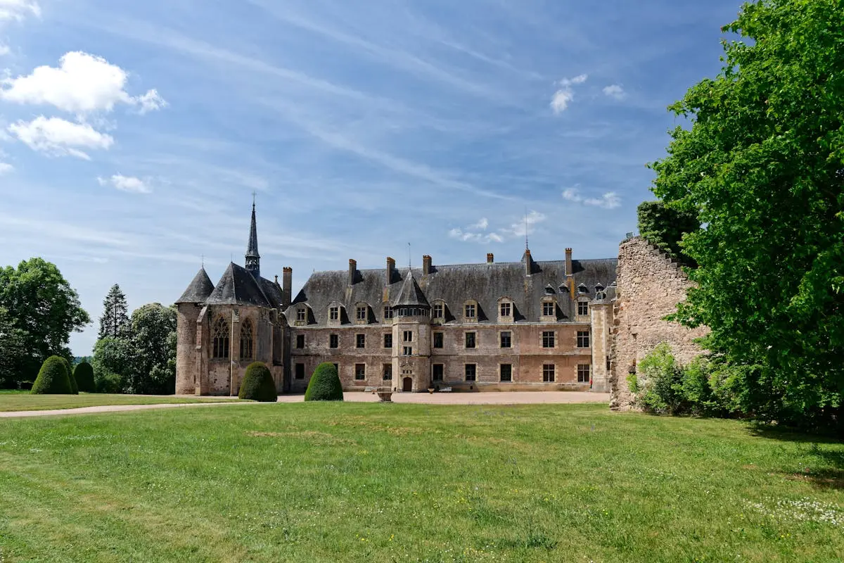 A stunning view of a historic castle in Lapalisse, France surrounded by lush greenery and blue skies.