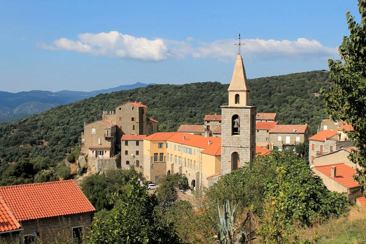 Picturesque village with stone buildings and bell tower against mountain backdrop.