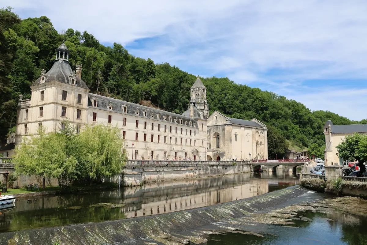 Brantôme Abbey in France with scenic river view and lush greenery.