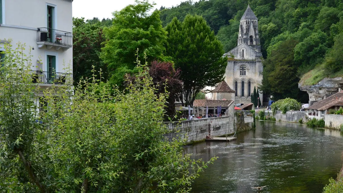 Picturesque scene of Brantôme Abbey by a tranquil river surrounded by lush greenery.