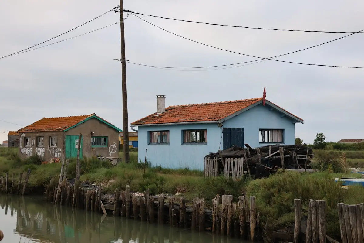 Charming rustic houses with orange roofs by a serene canal on a cloudy day.