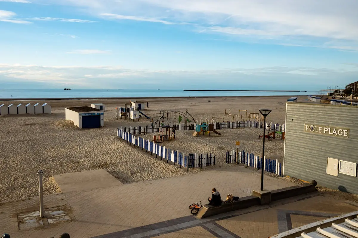 A serene beach scene at Boulogne-sur-Mer with a playground and beach huts under a clear sky.