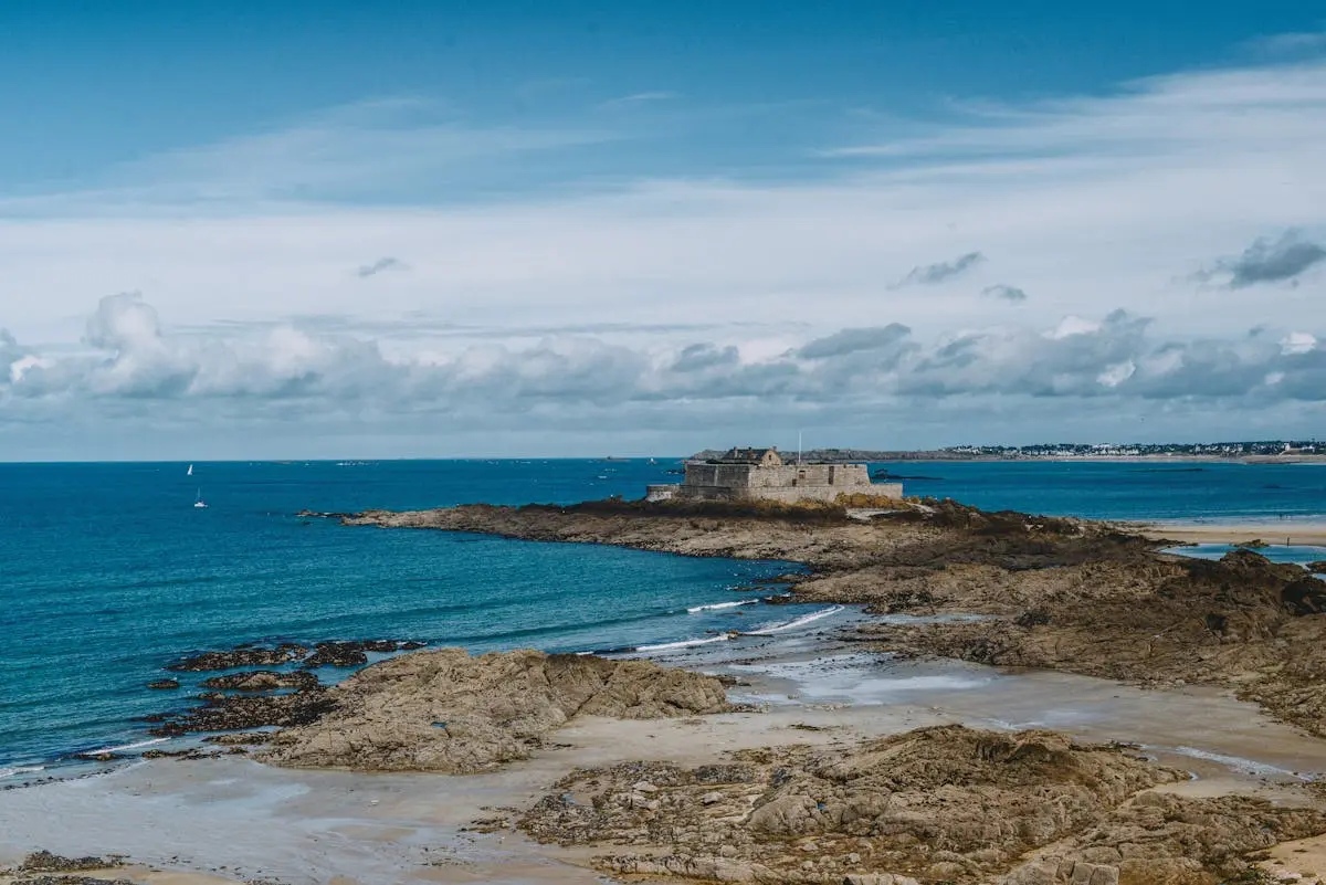 Breathtaking view of a historic fortress on the rocky coastline of Saint-Malo, France under a vibrant blue sky.