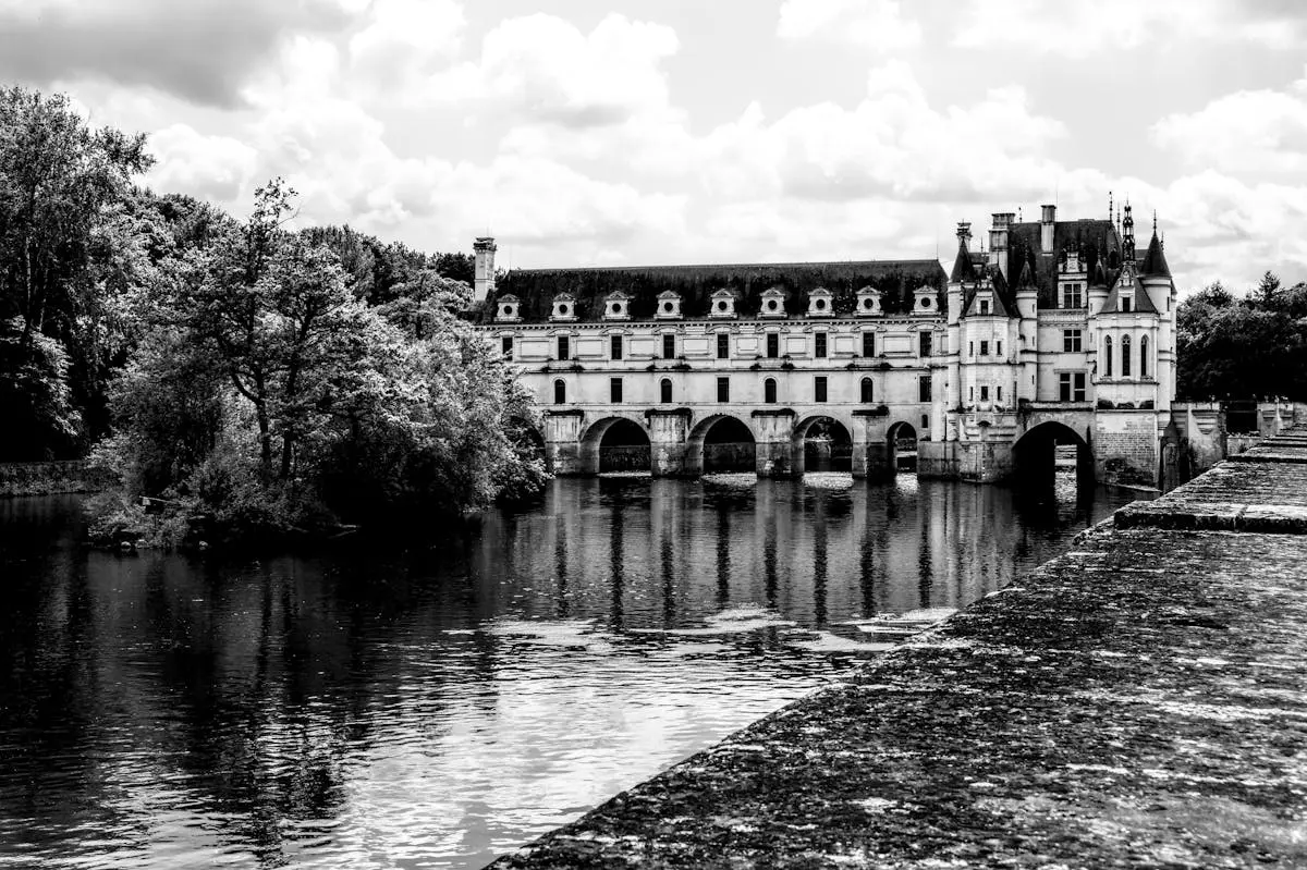 Dramatic black and white photo of Château de Chenonceau with reflection in river.